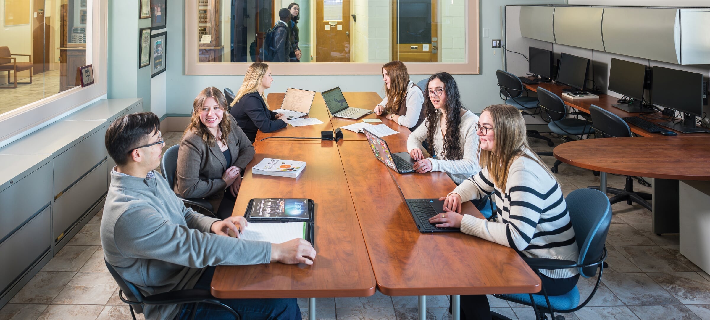 Six students sitting around a conference room table with laptops and notebooks.