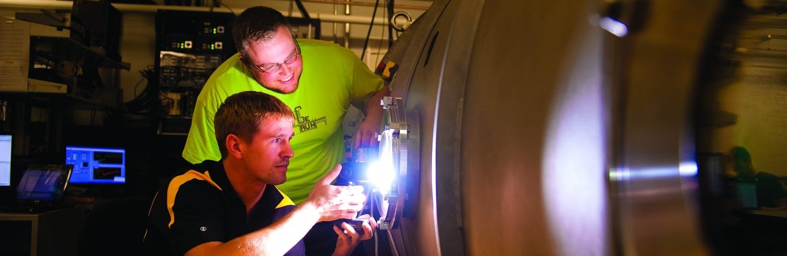 One Michigan Tech student welds thrusters onto a rocket, while another student watches.