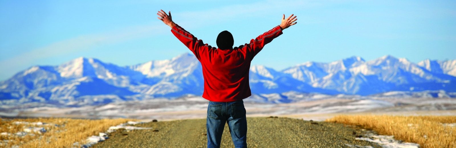 A man stands on a road, hands stretched towards the sky.