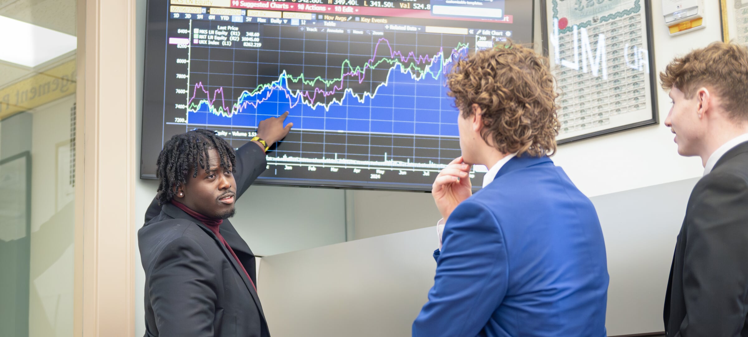 Three business students review data on a large screen.