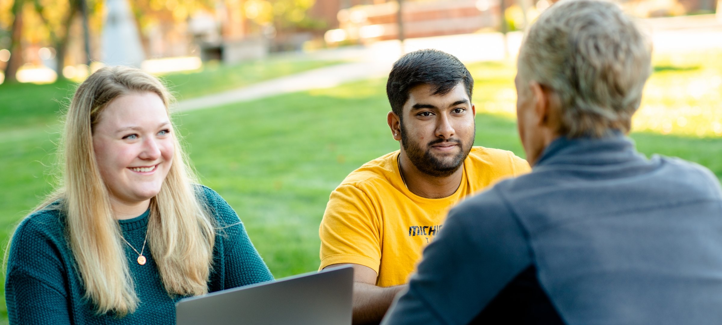 Two students sitting with a faculty member outside.