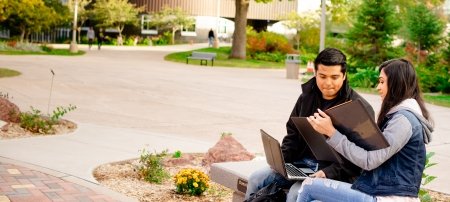 Students sitting on a bench outside on campus