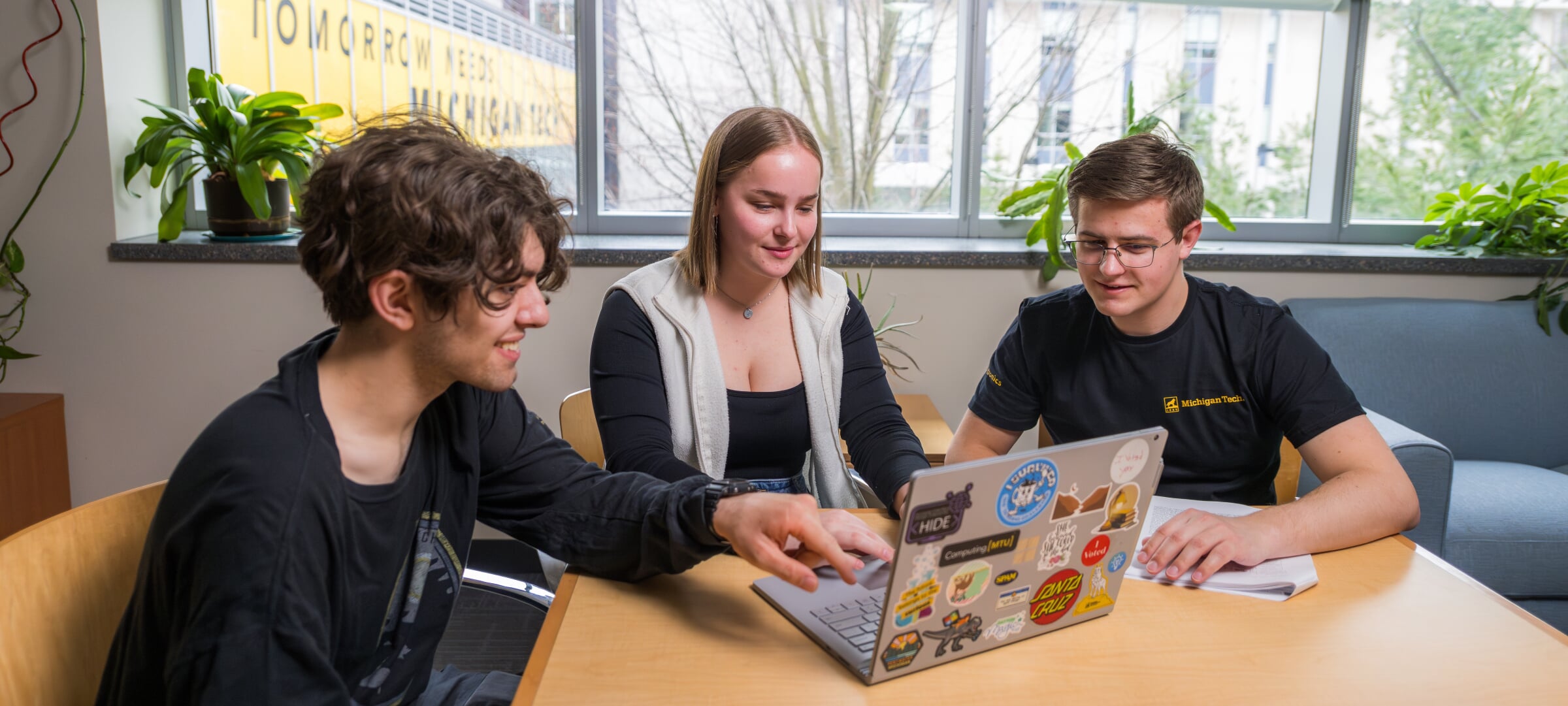 Three students looking at a laptop with one pointing at it