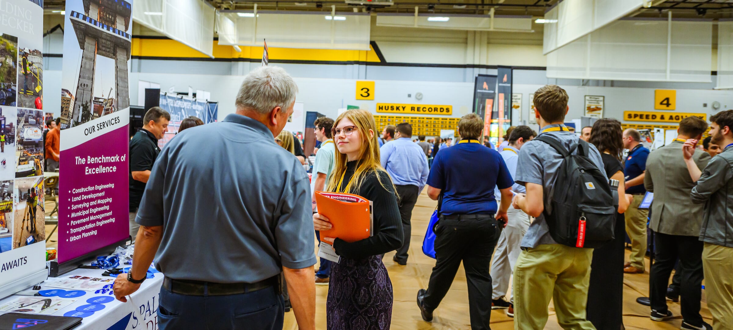 People are attending a bustling career fair inside a gymnasium.