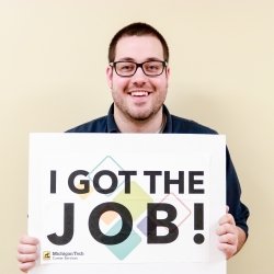 Student holding a sign that reads, "I got the job."