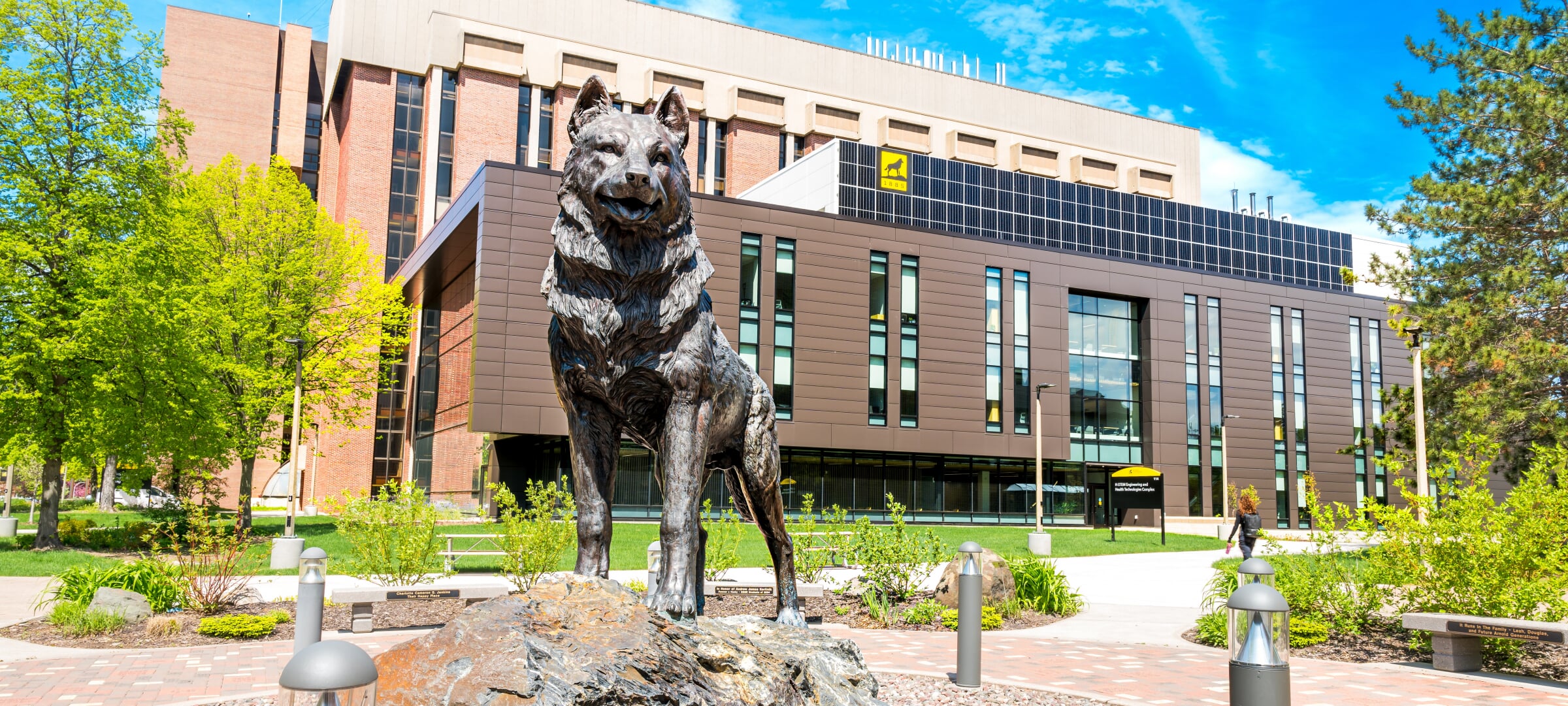 The Husky statue stands in front of a blue sky and a building on Michigan Tech's campus