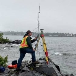 Student using surveying equipment on a shoreline.