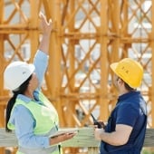 Two people in hard hats discussing a wooden structure being built.