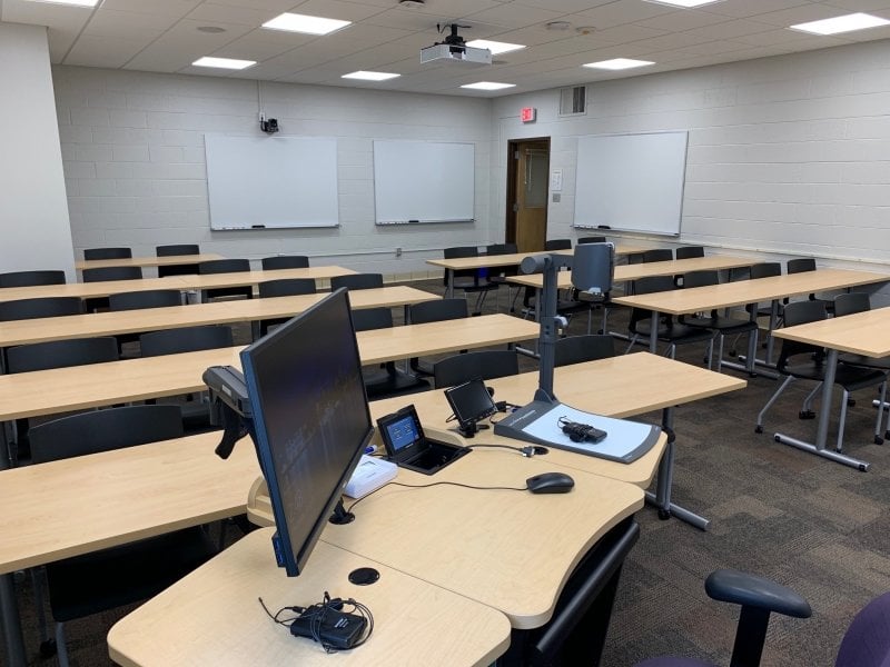 Dillman 204 showing 9 long bench tables with chairs on wheels. Three white boards are mounted on the walls.