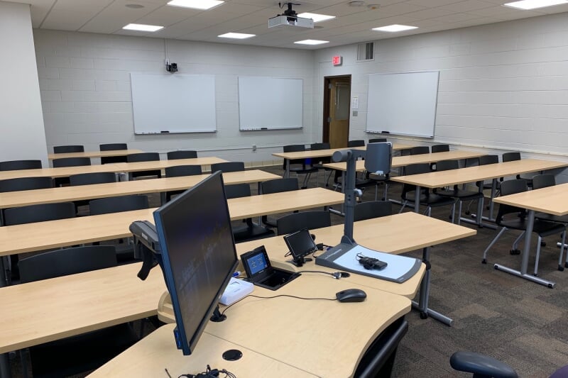 Dillman 204 showing 9 long bench tables with chairs on wheels. Three white boards are mounted on the walls.