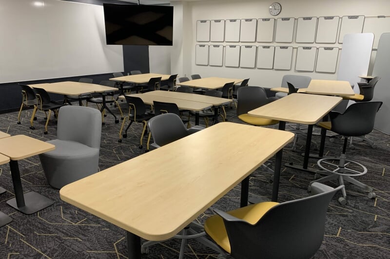 EERC 218 showing 3 tall tables, several pairs of shorter tables, and a variety of chairs with wheels. Individual white boards are hanging on the wall.