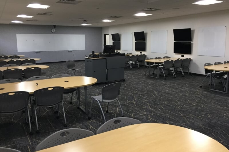 EERC 229 showing 9 tables with 6 chairs each arranged around the room. Each table has a pair of stacked monitors and white board on the wall