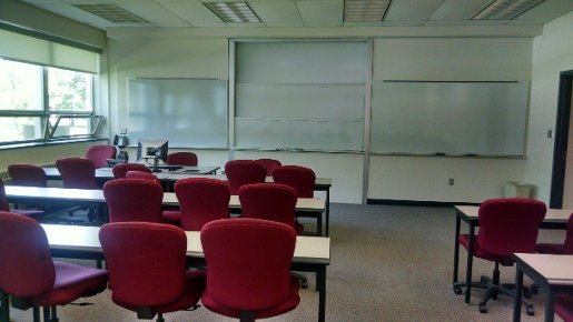 Fischer 125 showing long rectangular tables with office-style chairs on wheels facing a wall with whiteboards and lecture station.