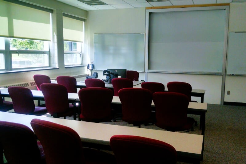 Fisher 125 showing long rectangular tables with office-style chairs on wheels facing a wall with whiteboards and lecture station.