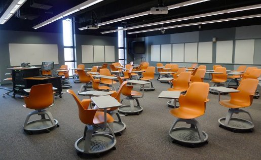 MEEM 402 showing a number of tablet-arm chairs with casters spread throughout the room.