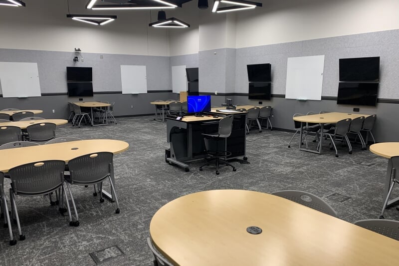 Rekhi G06 showing 9 student tables around the edge of the room, with monitors and white boards, and central lecture station.