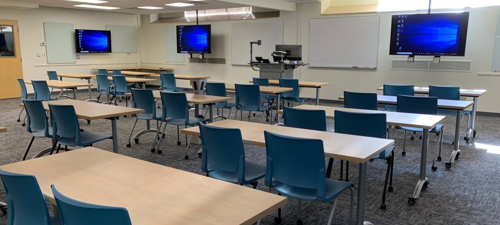 Wads G42 showing 14 short rectangular tables, each with 2 chairs, facing a wall with alternating whiteboards and monitors.