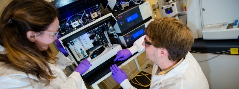 Two researchers in front of a piece of lab equipment.