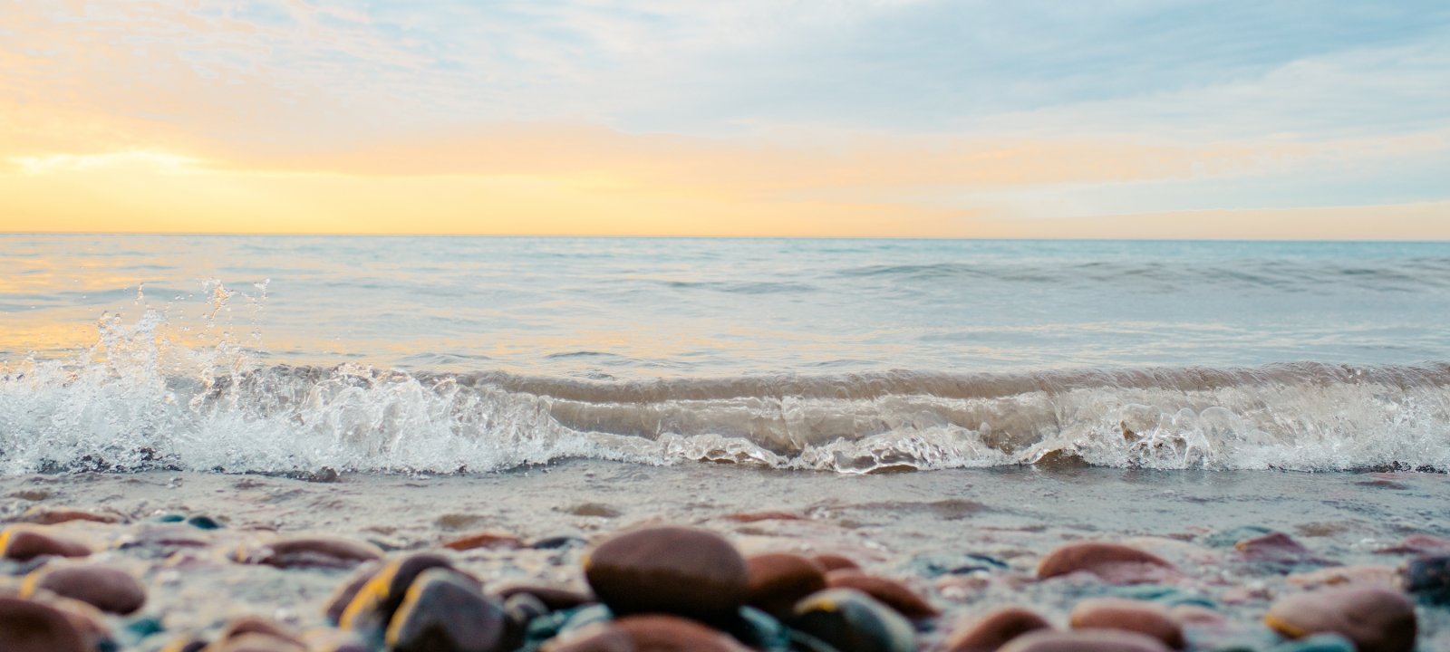 Alumni page featuring local area rocky beach, waves, lake, and sunset.