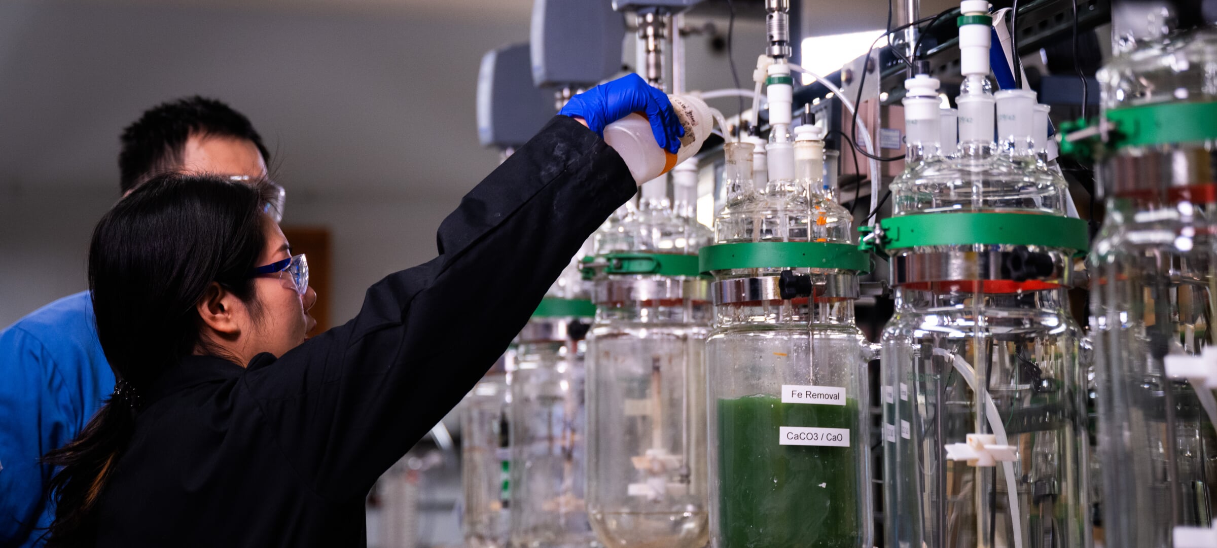 Two people in a lab and using large glass containers