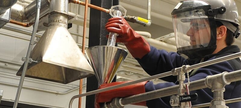 A person in protective equipment using a beaker and a funnel