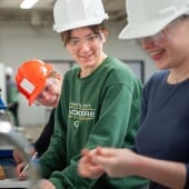 Students in safety glasses and hard hats smiling in a lab.