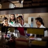 Graduate students working in a lab with safety glasses, lab coats, and gloves.