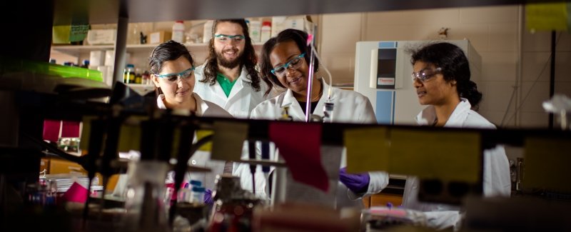 Graduate students working in a chemistry lab with safety glasses, lab coats, and gloves.