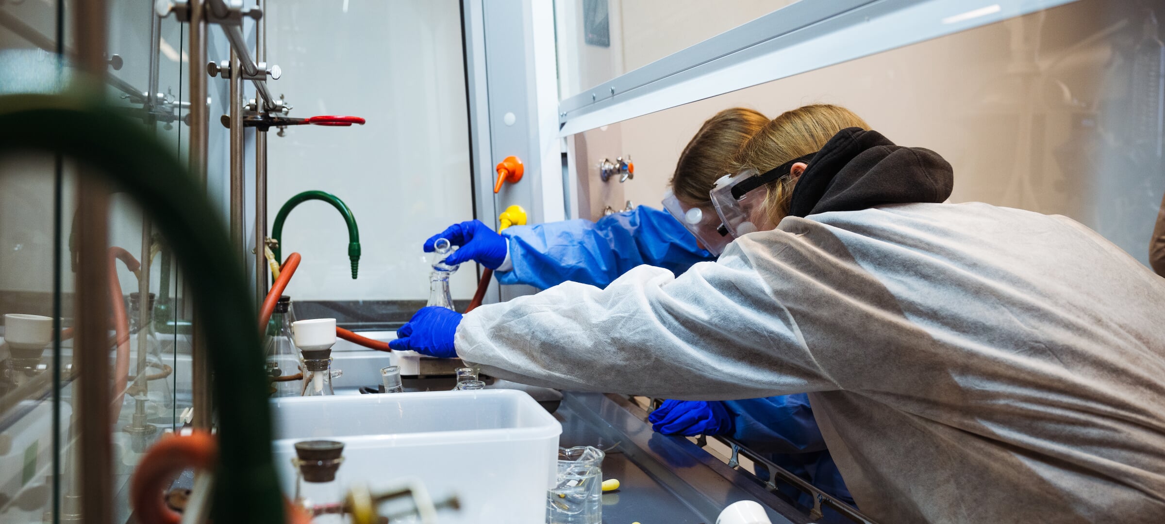Graduate students working in a chemistry lab with safety glasses, lab coats, and gloves.