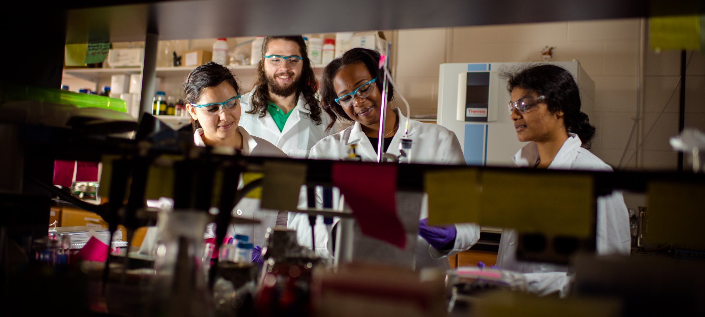 Graduate students working in a chemistry lab with safety glasses, lab coats, and gloves.