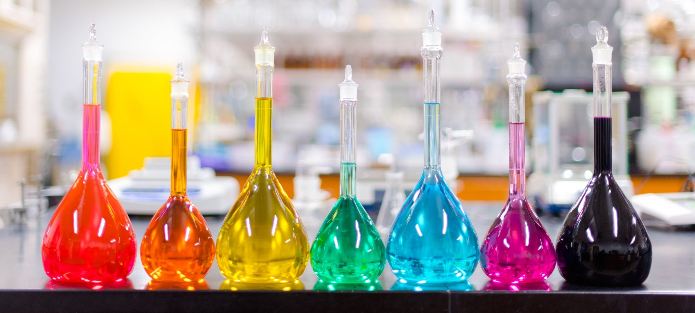 Colored filled barometers lined up in a row on a lab counter top