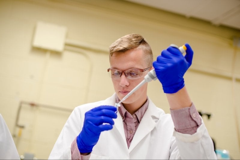 Student researcher using a pippet with goggle and lab coat