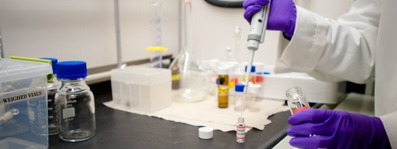 Contents of a vial being transferred via pipet by chemist wearing purple gloves