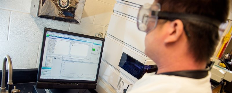 Student in a lab, wearing a white lab coat, working on a computer. 