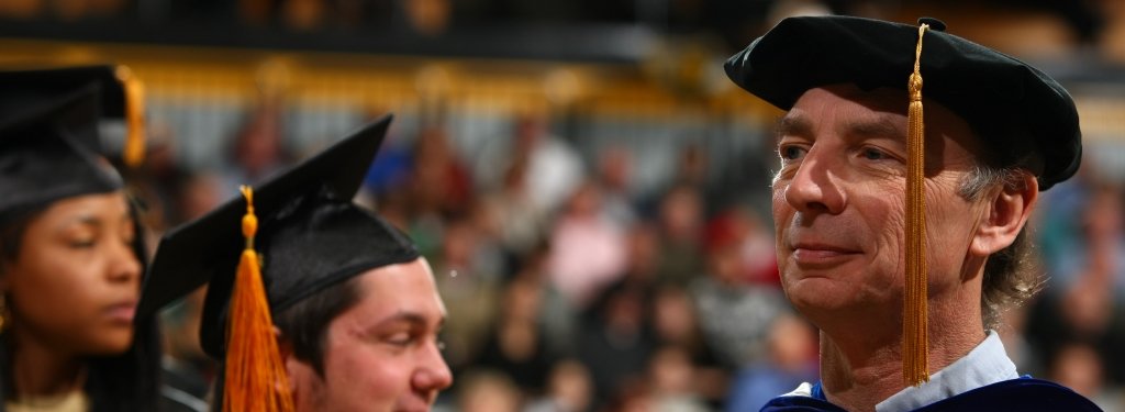 Two students stand next to Brad Baltensperger at commencement.