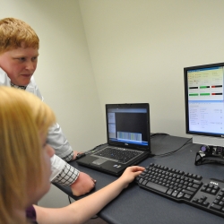 Two students interacting at a computer, one sitting and one is standing.
