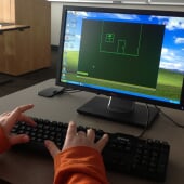 Hands typing on a keyboard with a line drawing on a monitor.