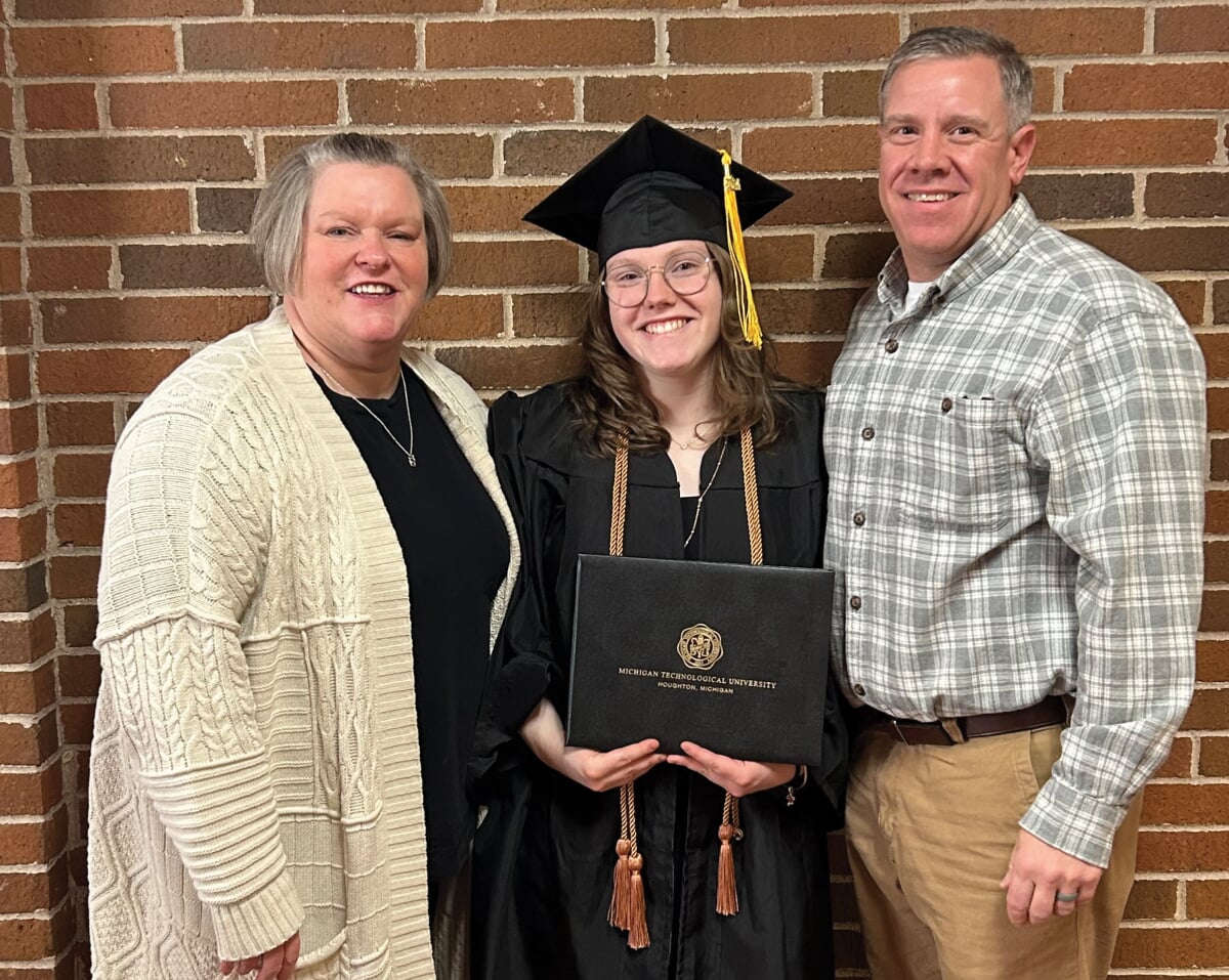 Abby Jurewicz wearing cap and gown, holding her diploma, with her parents.