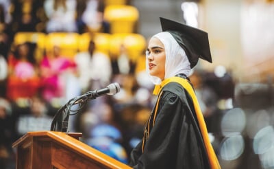 Tabasum Hamdard in commencement regalia at a podium.