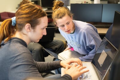 Two students working together on laptops.