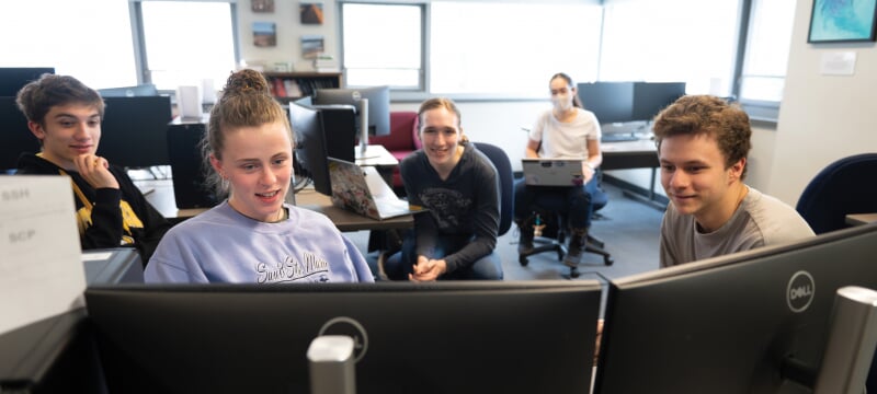 Four students looking at a computer in a computer lab.