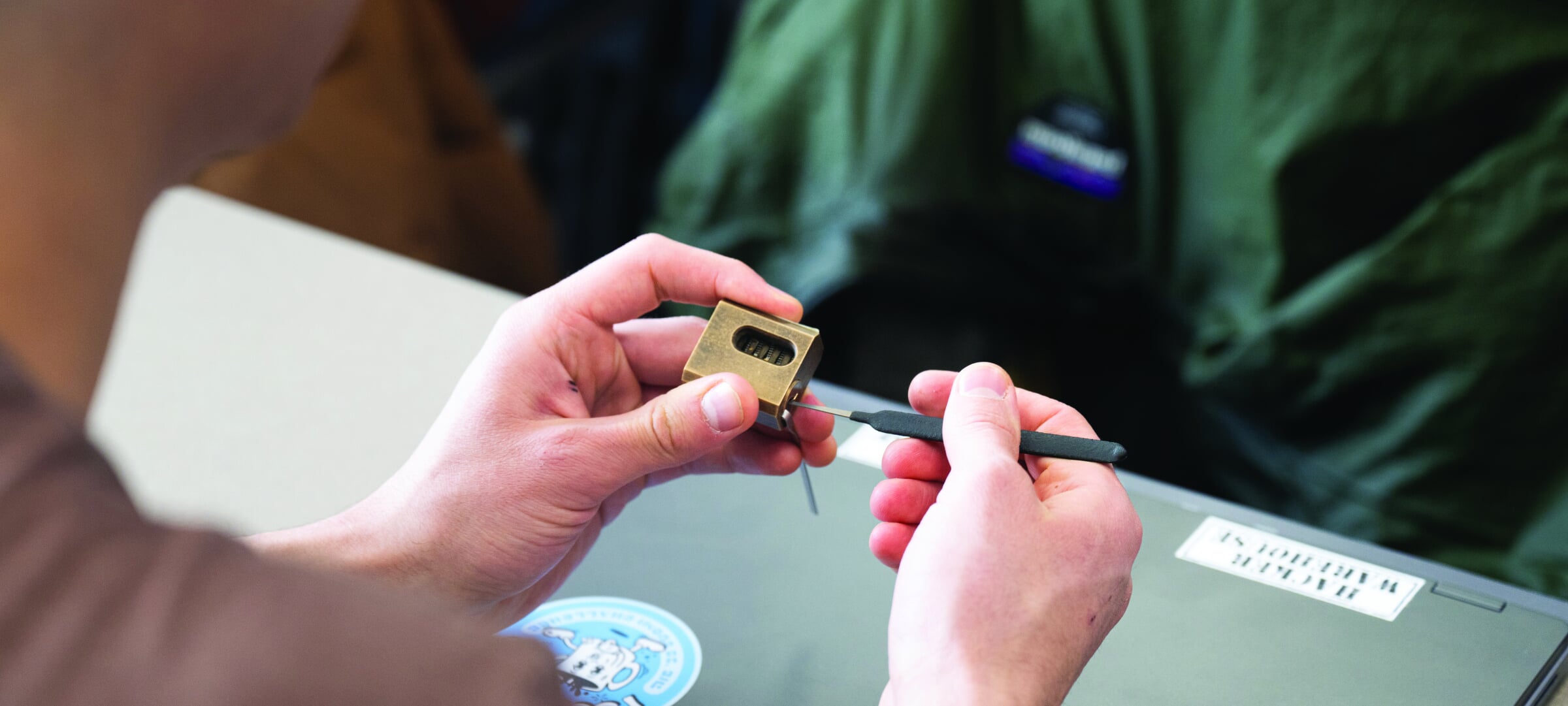 Hands using a lock pick on a padlock.