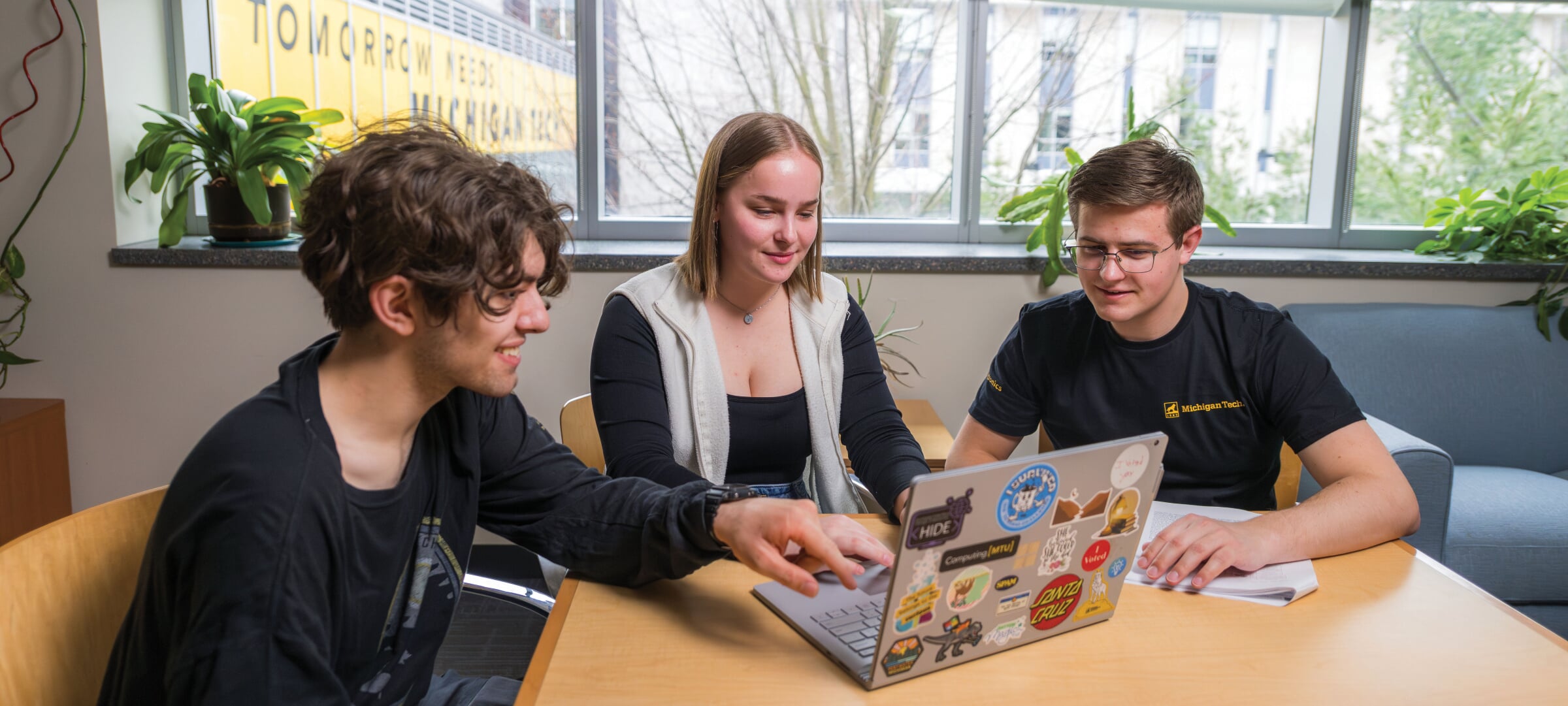 Three students sitting at a table looking at a laptop.