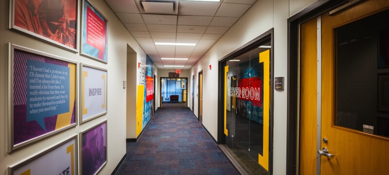Looking down a hallway in the College of Computing with posters on the wall, one saying Inspire, and a server room on the right.