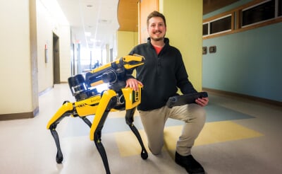 Michael Walker kneeling next to Balto, the robot dog.