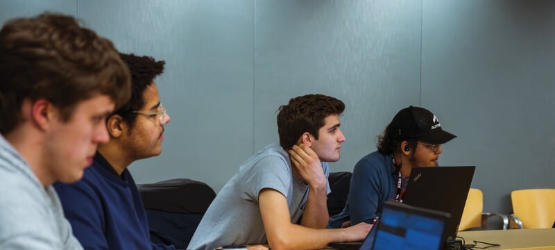 Students with laptops sitting at a desk.
