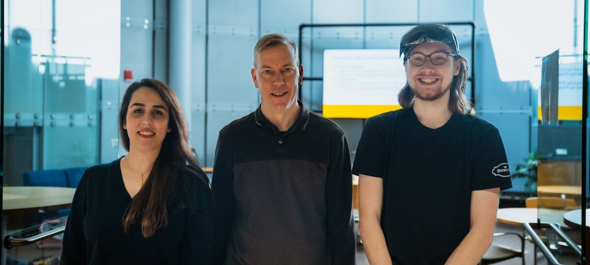 Three researchers standing in front of the doorway to a study lounge.