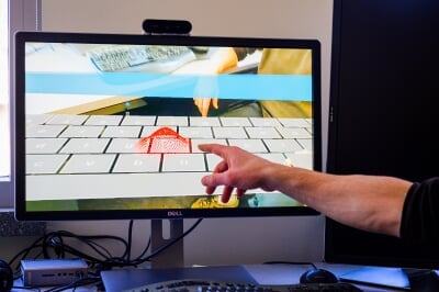 A hand points to a red-dotted area on a computer screen.