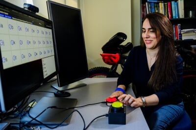 Soufia Bahmani pushes a red and a neon-yellow pushbutton with characters on the computer screen in front of her in an office setting.