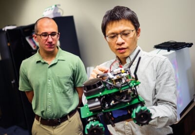 Bo Chen holding a small robot while Josh Dafoe looks on.